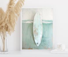 a surfboard is hanging on the wall next to a vase with dry grass in it