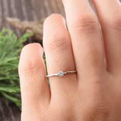 a woman's hand with a diamond ring on top of her finger, next to a plant