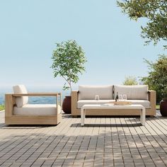 a couch and table on a wooden deck overlooking the ocean with a tree in the foreground