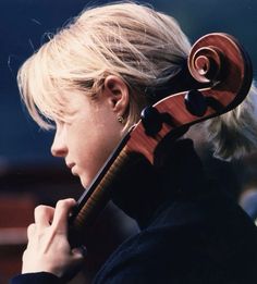 a woman with blonde hair holding a violin in her hand and looking at the side