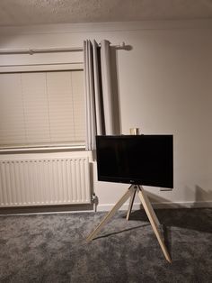 a flat screen tv sitting on top of a tripod in front of a window