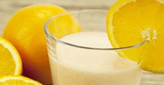 an orange smoothie in a glass next to sliced oranges on a wooden table