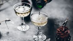 champagne being poured into two wine glasses on top of a table next to an assortment of desserts