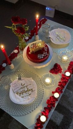 a table topped with plates covered in red roses and candles next to a cake on top of a plate