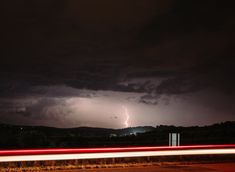 a lightning bolt is seen in the distance as it lights up the night sky over a rural area