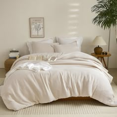 a bed with white sheets and pillows in a room next to a potted plant