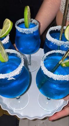 two blue margaritas with lime wedges and sugar on the rim are sitting on a white plate