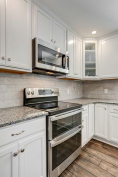 Kitchen Remodel with large kitchen island with additional seating, storage, and counter space, bright white cabinets accompanied with gray granite countertops, white brick backsplash, and brown vinyl plank floors Black Countertops White Cabinets Backsplash Ideas, White Kitchen Gray Granite Countertops, Kitchen Cabinets Colors For 2023, White Cabinet Gray Granite Countertop, White Kitchen Cabinets With Grey Granite, Kitchen Backsplash With White Cabinets And Grey Granite, Backsplash White Cabinets Grey Counter, Lvp With White Cabinets, Backsplash With White Granite Counters