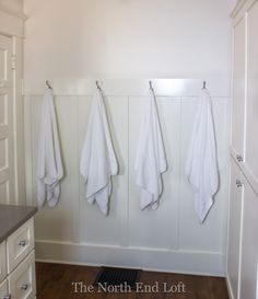 three white towels hanging on the wall in a bathroom with wood flooring and cabinets