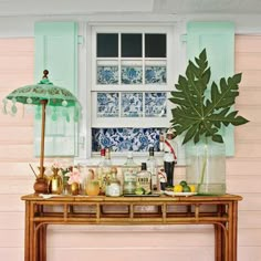 a wooden table topped with lots of bottles and glasses next to a window covered in green shutters