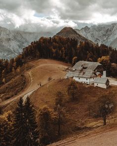 an old barn sits on the side of a hill with mountains in the back ground