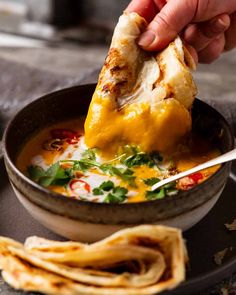 a person dipping some food into a bowl with tortilla chips on the side