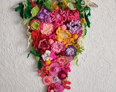 a bunch of crocheted flowers hanging on the wall in front of a white wall