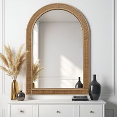 a mirror sitting on top of a white dresser next to a vase with dried grass