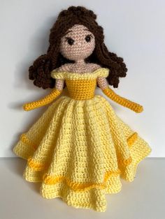 a crocheted doll in a yellow dress on a white surface with one hand