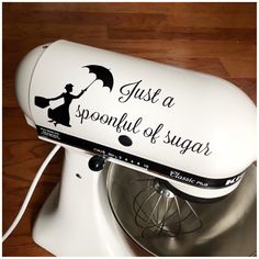 a white mixer sitting on top of a wooden floor next to a sign that says just a spoonful of sugar