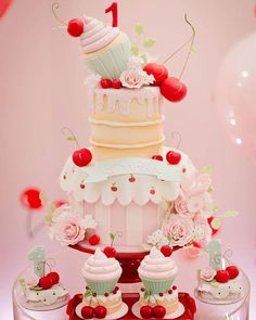 a three tiered cake and cupcakes on a table