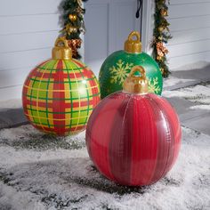 two christmas ornaments sitting on top of snow covered ground next to a door and wreath