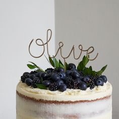 a white cake with blueberries and greenery on top that says love in cursive writing