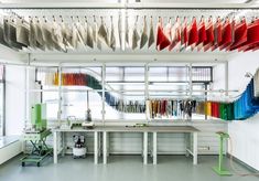 a room with many different colored shirts hanging from the ceiling and two tables in front of them