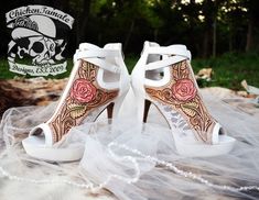 a pair of white high heeled shoes decorated with roses and skulls on the side