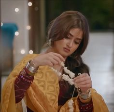 a woman in a yellow and red sari is holding some white beads while she looks down at her hand