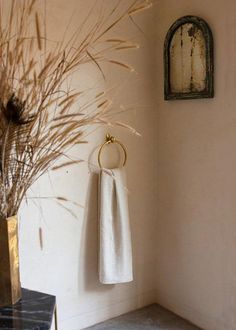 a white towel hanging on the wall next to a vase with dry grass