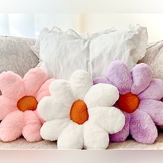 three stuffed flowers sitting on top of a couch next to pillows and pillowcases