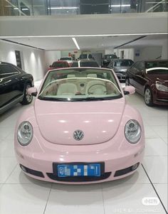 a pink vw beetle convertible parked in a showroom next to other black cars