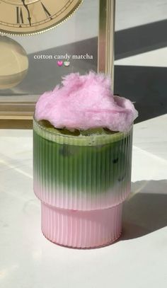 a pink and green cup sitting on top of a white table next to a clock