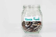 a glass jar filled with coins sitting on top of a white table next to a sign that says house fund