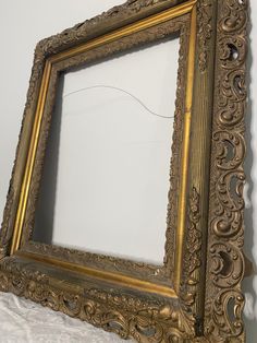 an ornate gold frame is hanging on the wall next to a white bedding sheet