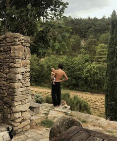 a man standing in front of a stone wall next to a forest filled with trees