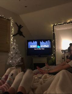 two people sitting on a bed in front of a flat screen tv with christmas lights