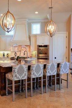 an image of a kitchen with chandeliers hanging from it's ceiling and chairs around the island