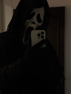 a person in a black hoodie holding a cell phone with a white mask on it