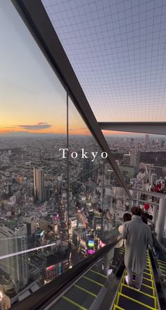 two people walking up the side of a tall building with tokyo in the background at sunset