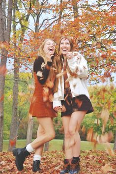 two young women standing next to each other in the leaves