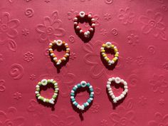 four beads are arranged in the shape of hearts on a pink background with swirls