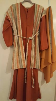 an orange dress hanging on a wall next to two coats and a coat hanger