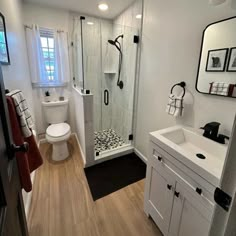 a white bathroom with black accents and wood flooring, along with a walk in shower