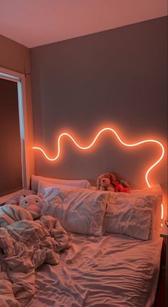 an unmade bed with white sheets and pillows in front of a neon light headboard