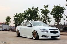 a white car parked in front of some trees on the side of the road with gold rims