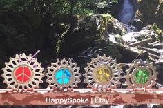 four colorful metal clocks sitting on top of a wooden bridge next to a river and waterfall