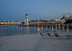 beach chairs are lined up on the sand near water and buildings in the background at night