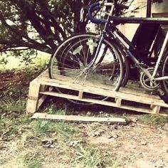 a bicycle parked on top of a wooden pallet in front of a tree and building