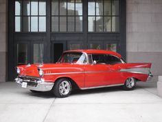 an old red car parked in front of a building