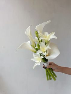 a bouquet of white flowers being held by a woman's hand in front of a wall