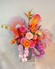 a vase filled with lots of colorful flowers on top of a white table next to a wall