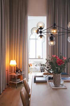 a dining room table with flowers in a vase on it and lights hanging from the ceiling